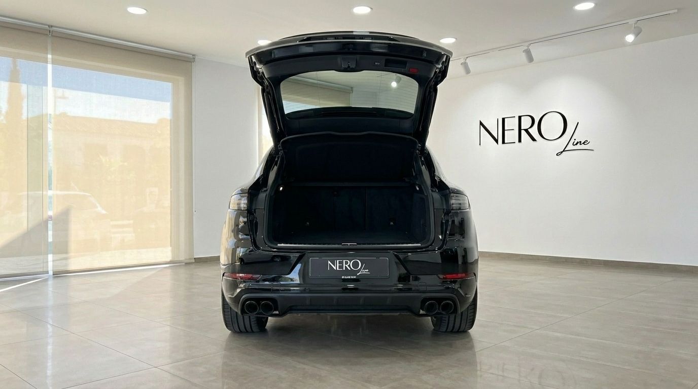 The black Porsche Cayenne is shown from the rear with its trunk open, parked in a bright showroom in Alicante.
