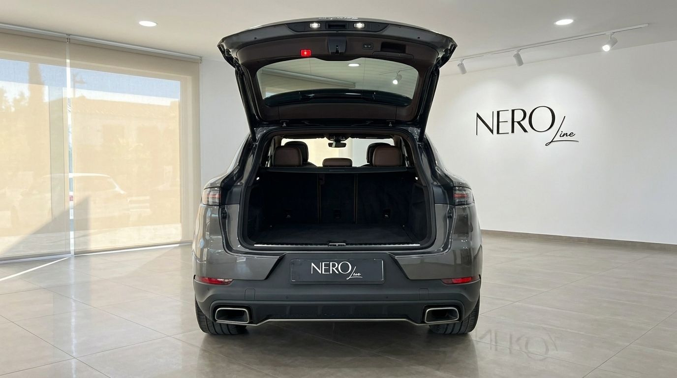 The rear view of a gloss Quarzite Grey Metallic Porsche Cayenne with its trunk open, showcasing the spacious cargo area and rear seats in Alicante.