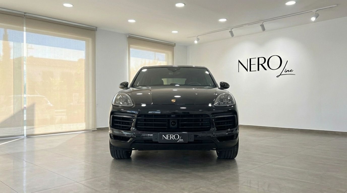 A black 2022 Porsche Cayenne is parked head-on in a bright showroom in Barcelona, showcasing its front grille and headlights.