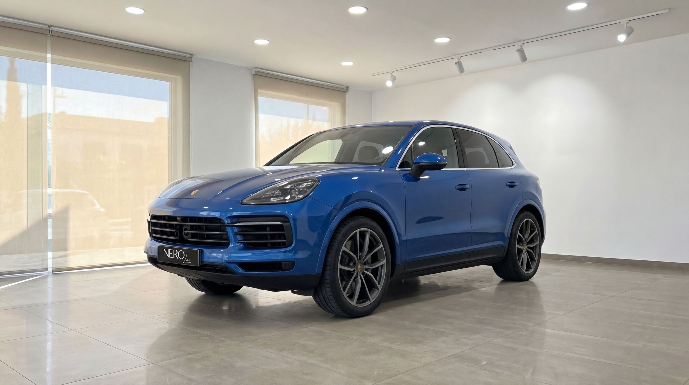 The blue 2024 Porsche Cayenne is showcased in a front three-quarter view inside a bright showroom in Mallorca.