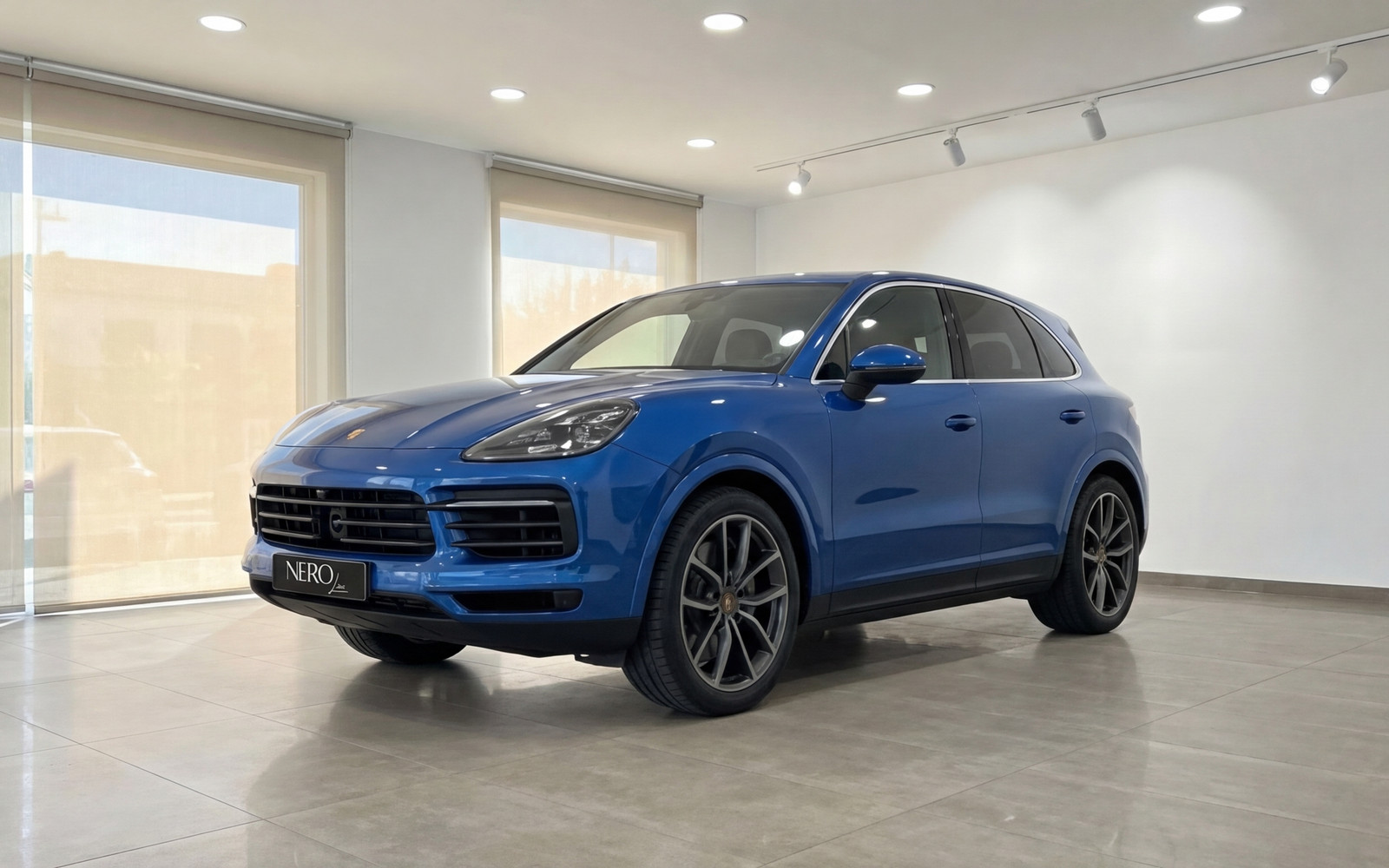 Porsche Cayenne — Blue SUV in Mallorca Showroom The blue 2024 Porsche Cayenne is showcased in a front three-quarter view inside a bright showroom in Mallorca.