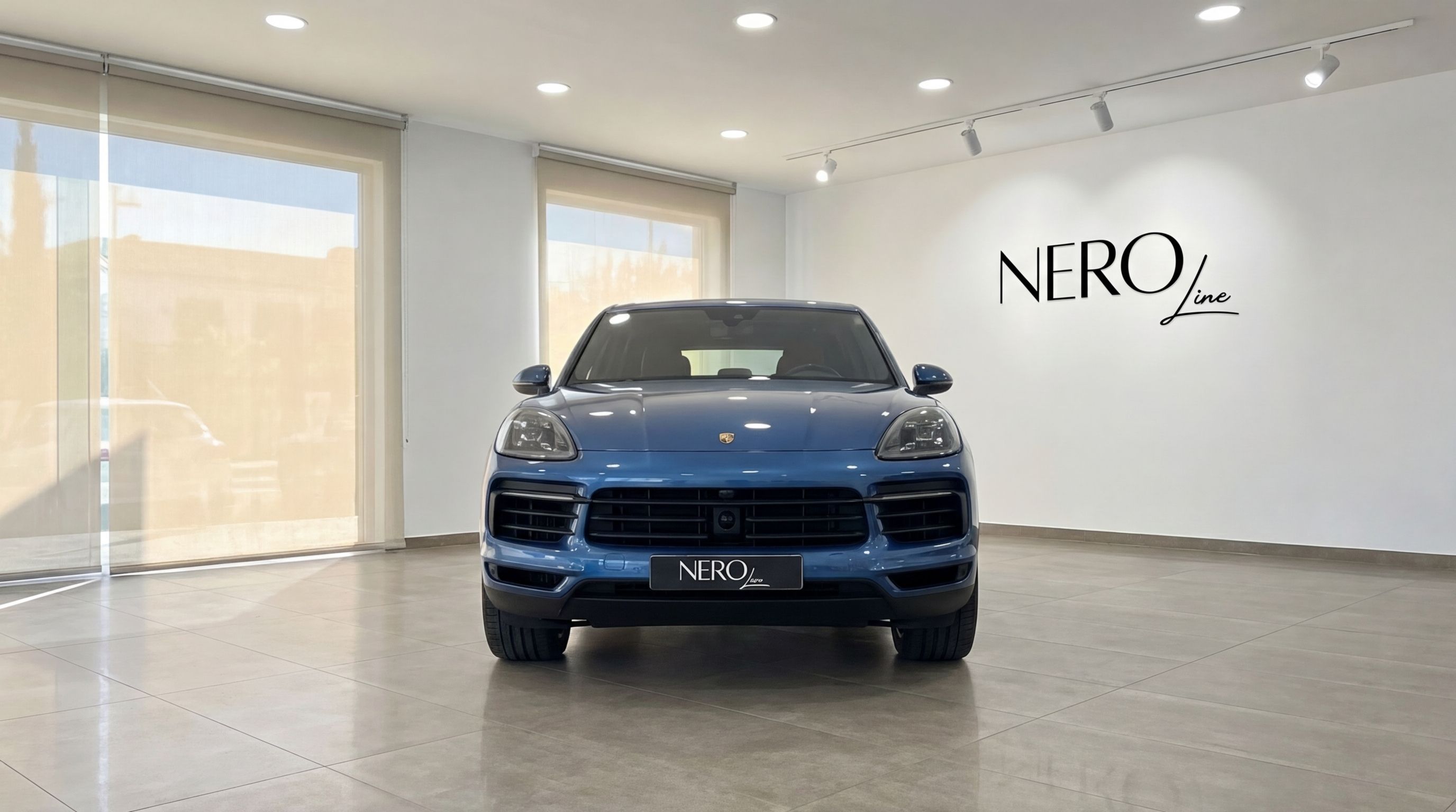 The blue Porsche Cayenne is prominently displayed from the front in a bright showroom in Mallorca, showcasing its elegant design.