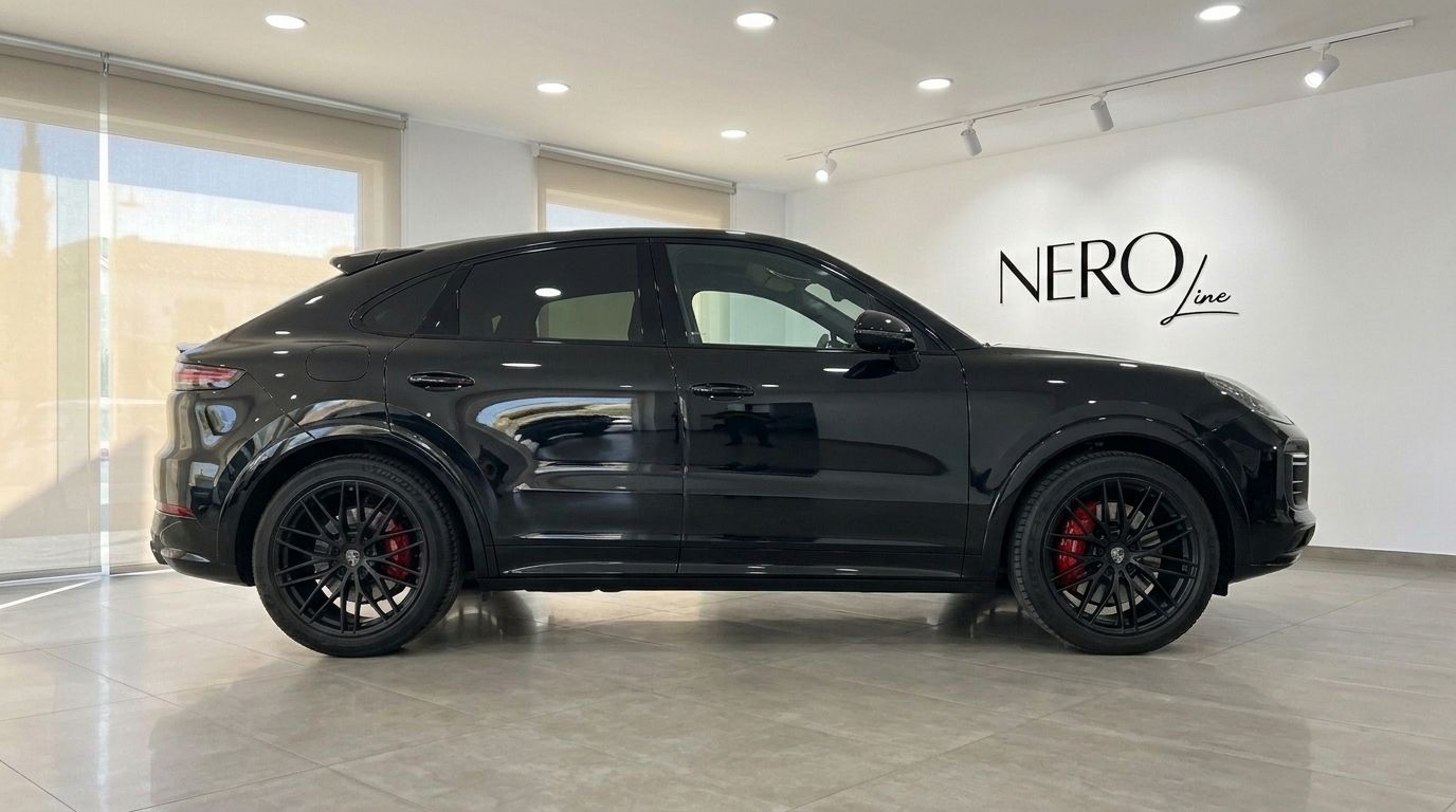 El Porsche Cayenne GTS negro brillante se muestra de perfil completo dentro de un concesionario en Alicante, destacando su diseño elegante y pinzas de freno rojas.