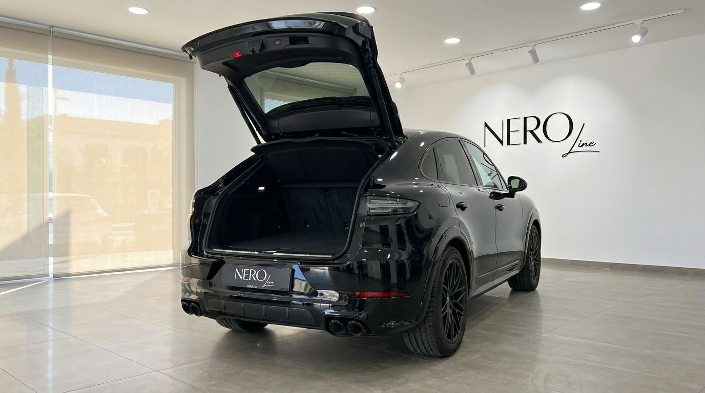 El Porsche Cayenne GTS negro se muestra desde la parte trasera con el maletero abierto, revelando un amplio espacio de carga en un concesionario en Alicante.