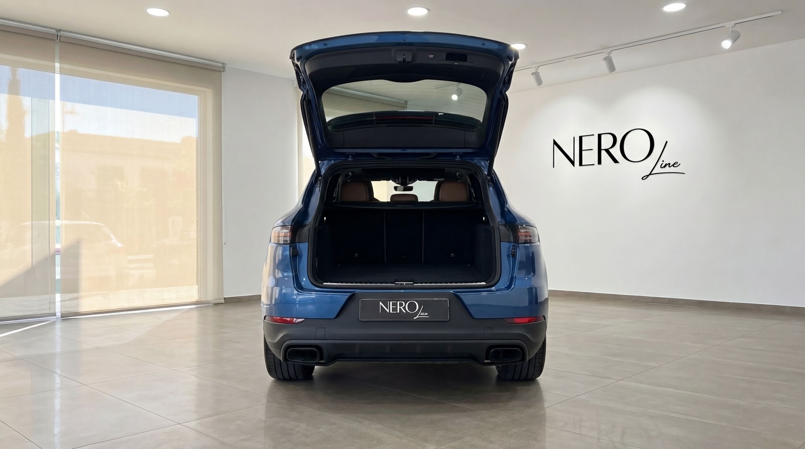 The blue Porsche Cayenne is shown from the rear with its trunk open, revealing the spacious interior in a Mallorca showroom.