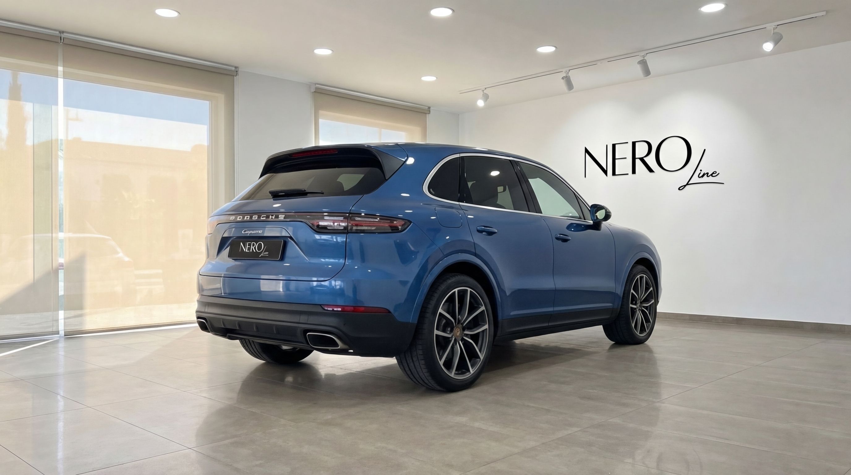 A blue Porsche Cayenne SUV is shown from a rear three-quarter angle, parked indoors in Mallorca.