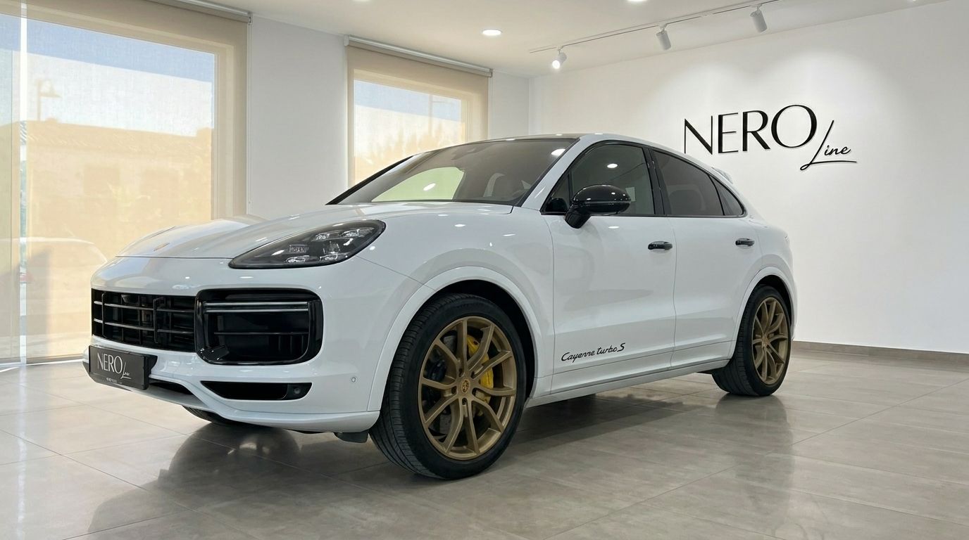 The white Porsche Cayenne Turbo S E-Hybrid is displayed in a showroom in Alicante, showing its front three-quarter view with gold wheels.