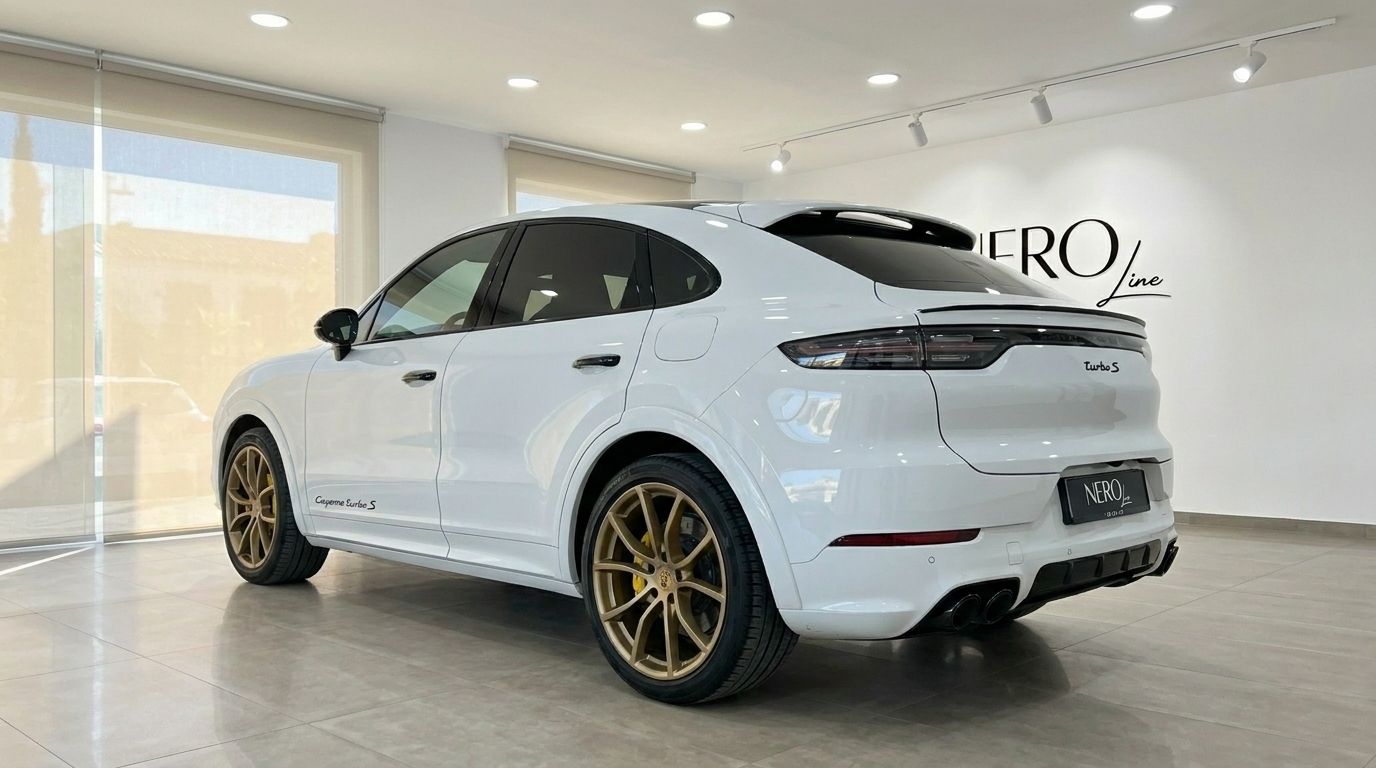 The white Porsche Cayenne Turbo S E-Hybrid is shown from a rear three-quarter angle with gold wheels in an Alicante showroom.