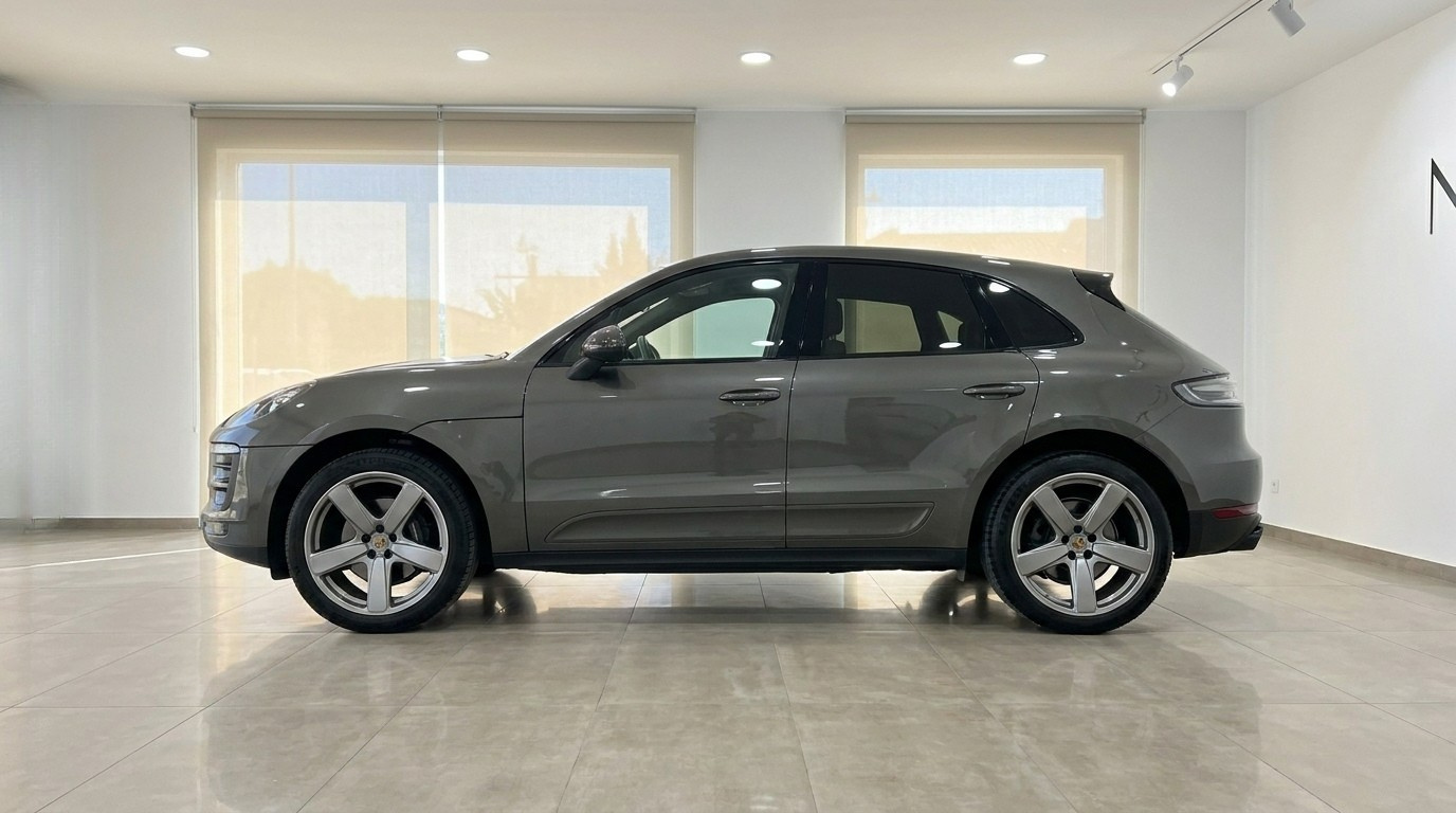A gloss Volcano Grey Metallic Porsche Macan 2.0 Turbo is displayed from its side profile in a showroom in Alicante.