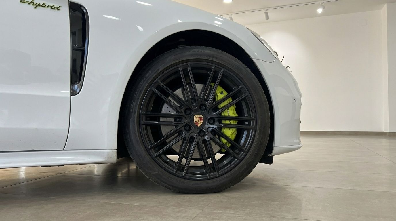 The front wheel of a white Porsche Panamera Turbo S Hybrid in Alicante, showcasing its black multi-spoke rim and vibrant green brake caliper.