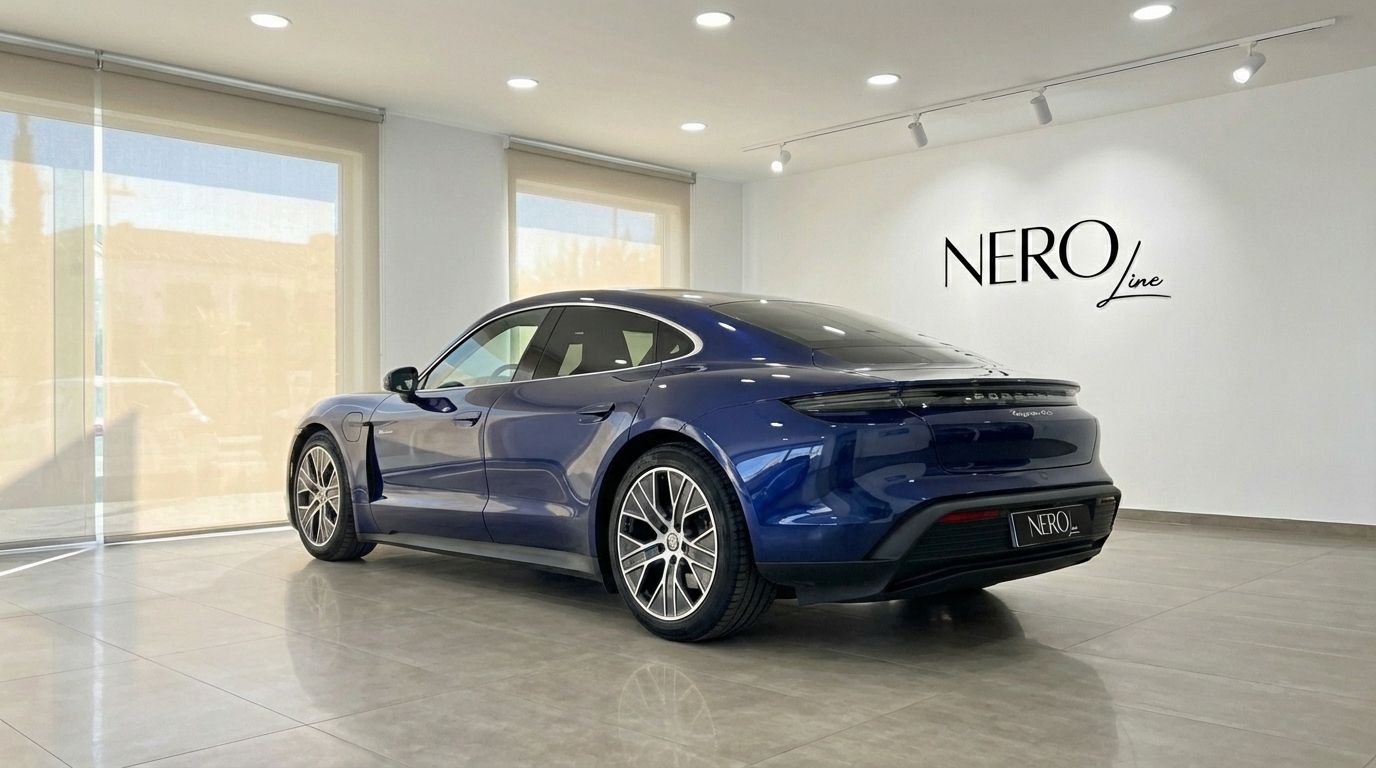 The blue Porsche Taycan 4S, a luxury electric sedan, is showcased from a rear three-quarter view in a showroom in Alicante.