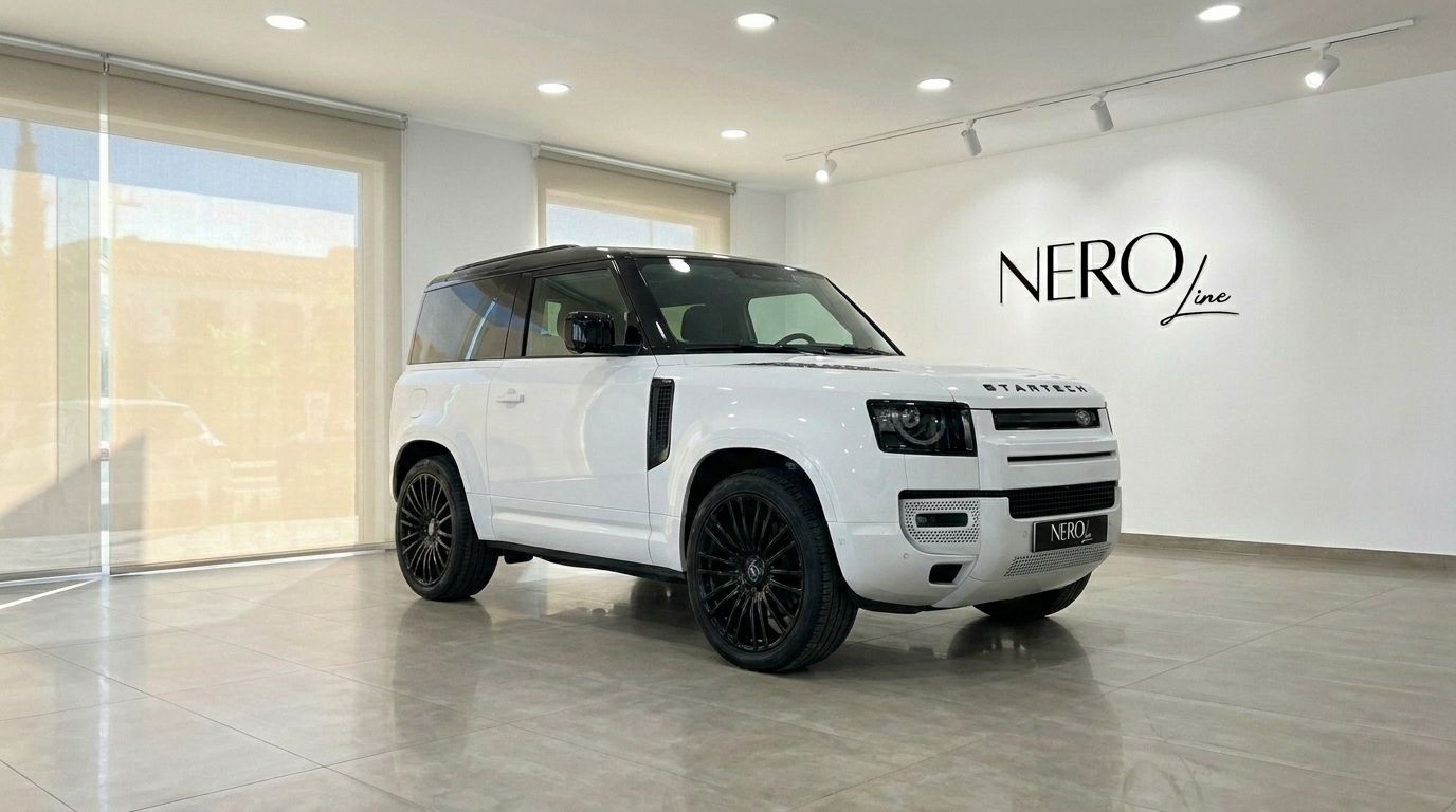 The white Range Rover Defender 90 Startech Edition is showcased from a front three-quarter angle in a modern showroom in Marbella.