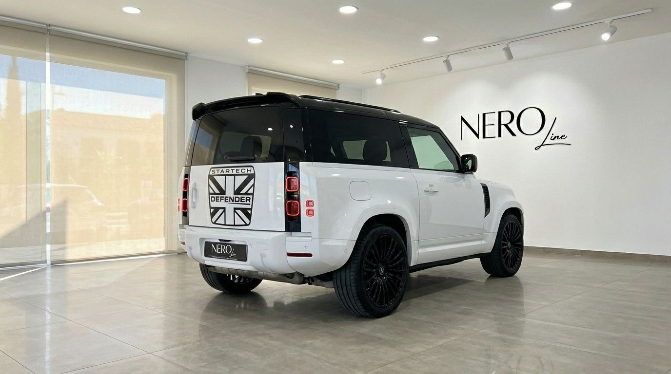 Der weiße 2024 Range Rover Defender 90 Startech Edition wird aus der hinteren Dreiviertelansicht in einem hellen Showroom in Marbella präsentiert.