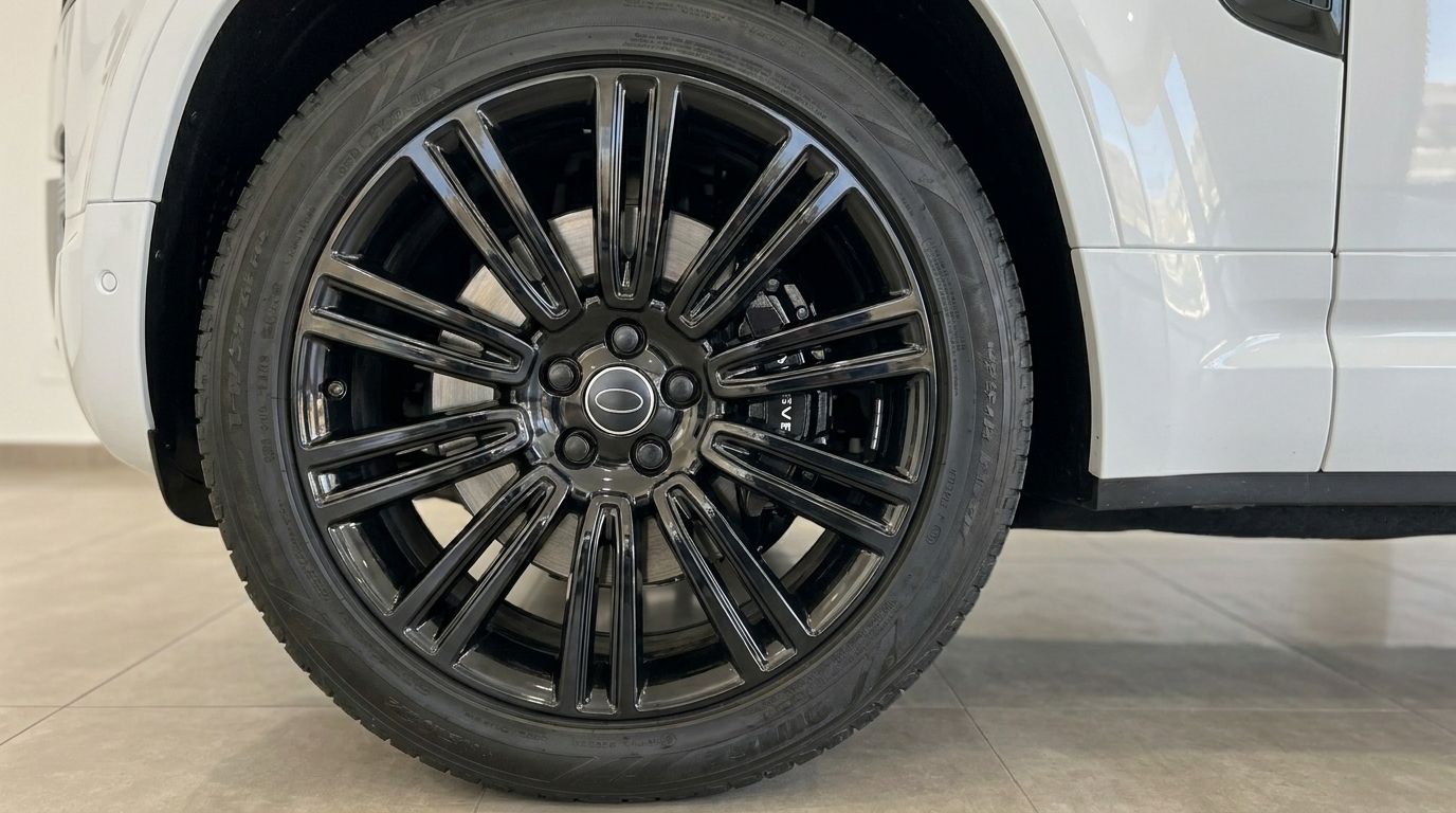 Nahaufnahme des glänzend schwarzen Mehrspeichenrads und Reifens des weißen Range Rover Defender 90 Startech Edition in Marbella.