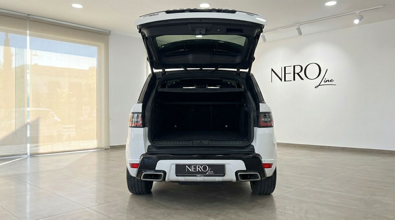 The white 2022 Range Rover Sport's rear view shows its open trunk, revealing a spacious cargo area inside a Barcelona showroom.
