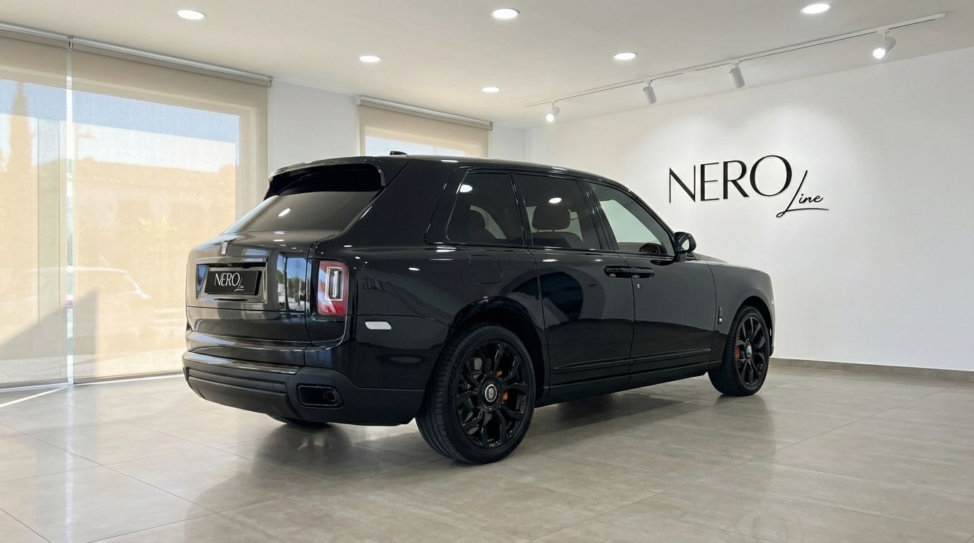 Un elegante SUV de lujo Rolls-Royce Cullinan negro de 2025 está estacionado en una sala de exposición moderna en Madrid, visto desde su ángulo trasero tres cuartos.