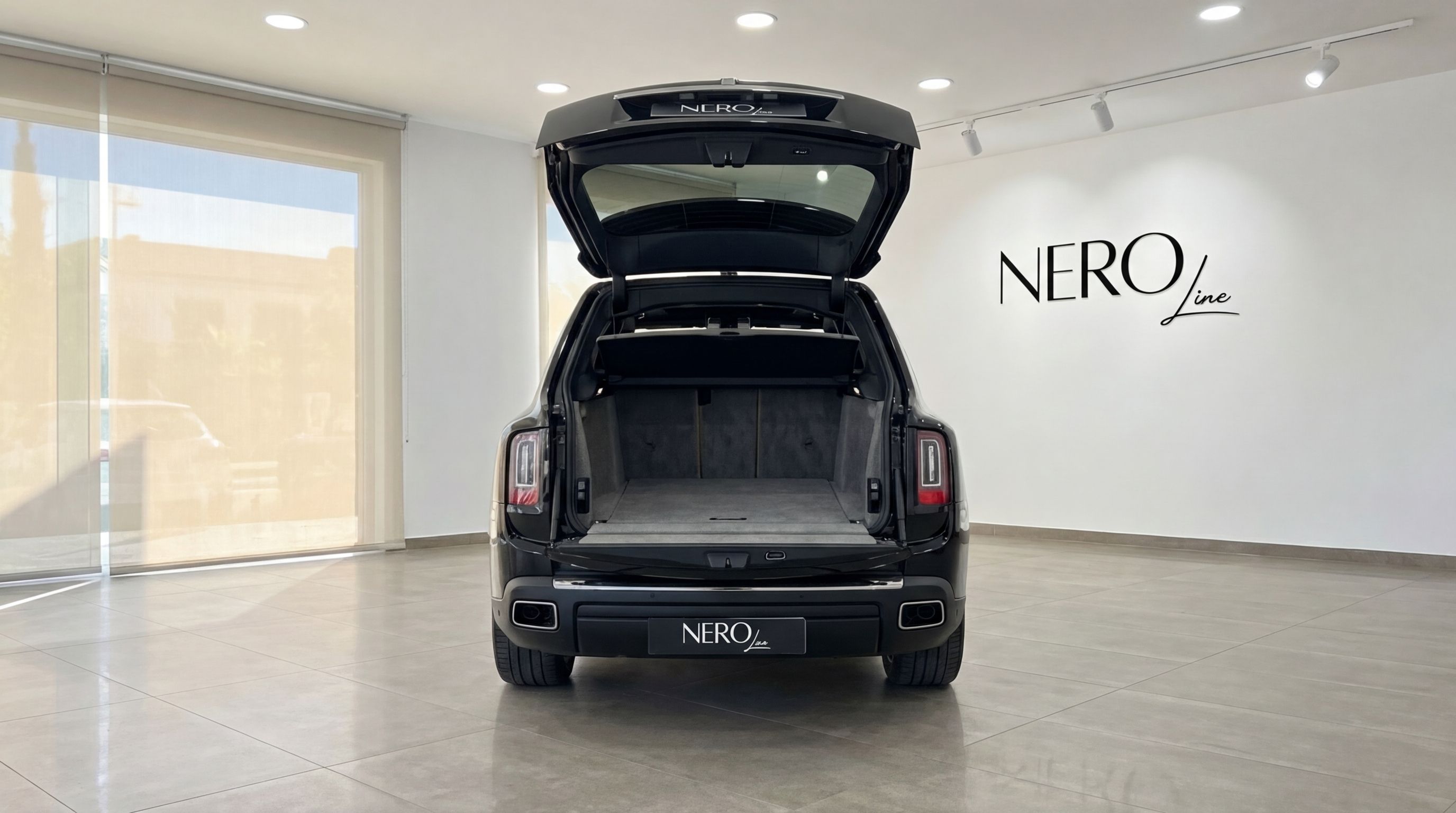 The rear view of a jet black Rolls-Royce Cullinan with its trunk open, showcasing ample cargo space in Ibiza.