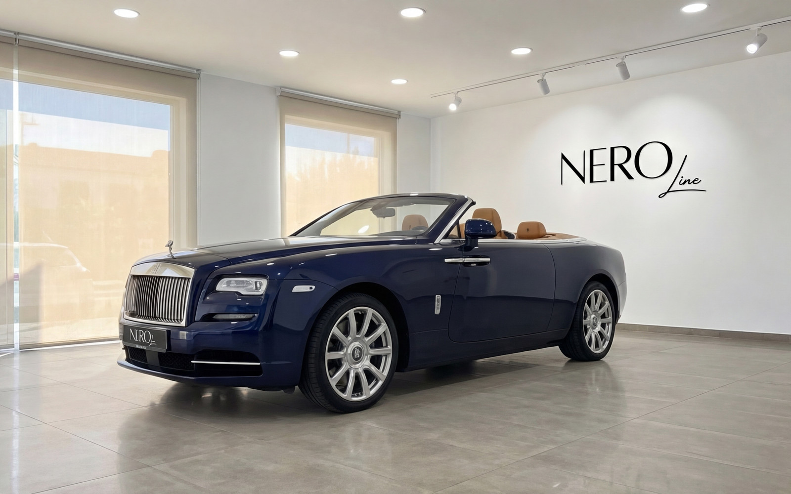 Rolls-Royce Dawn — Midnight Blue Convertible The midnight blue Rolls-Royce Dawn convertible with its top down and tan interior is showcased in a Barcelona showroom.
