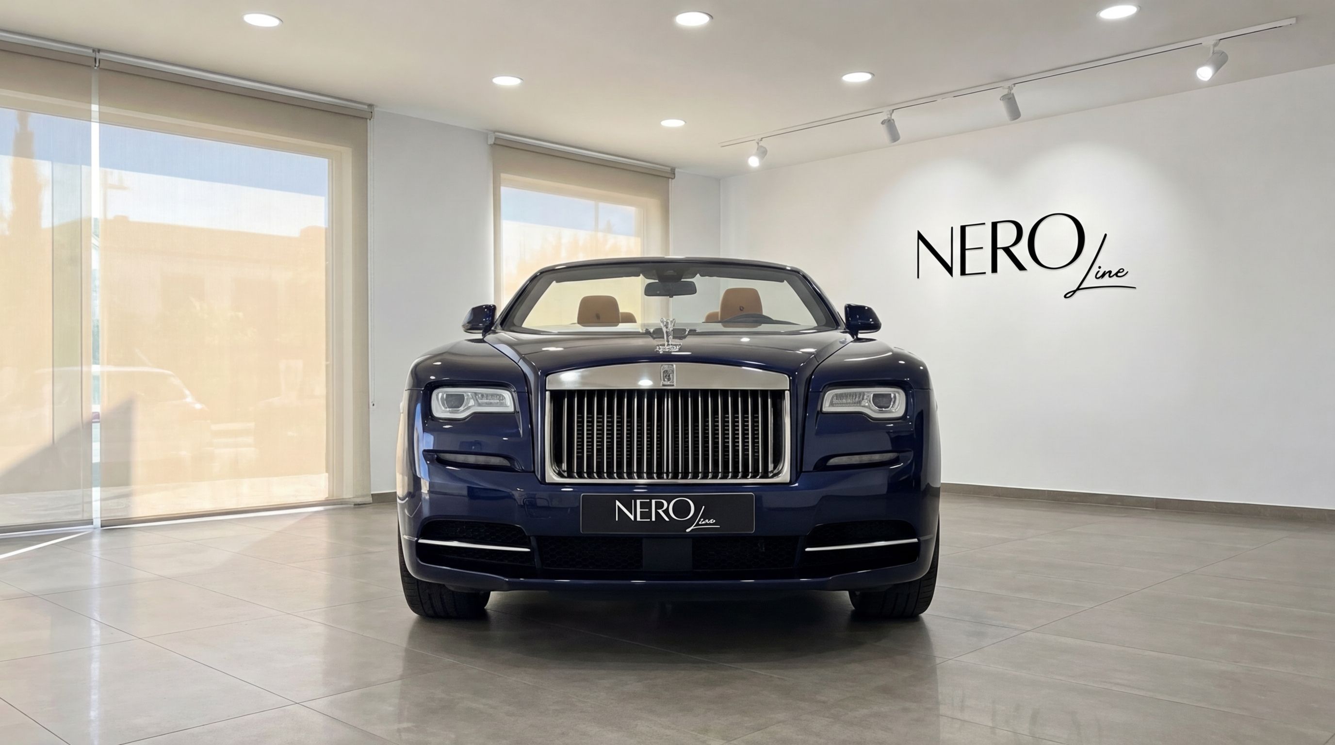 A midnight blue Rolls-Royce Dawn convertible, featuring a light brown interior, is prominently displayed from the front in a Barcelona showroom.