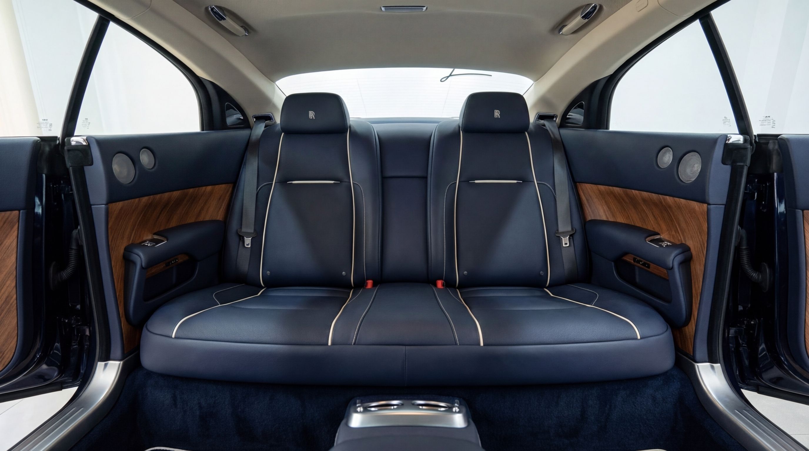 The rear interior of the Rolls-Royce Dawn in Barcelona, featuring luxurious midnight blue leather seats with white piping and elegant wood trim.