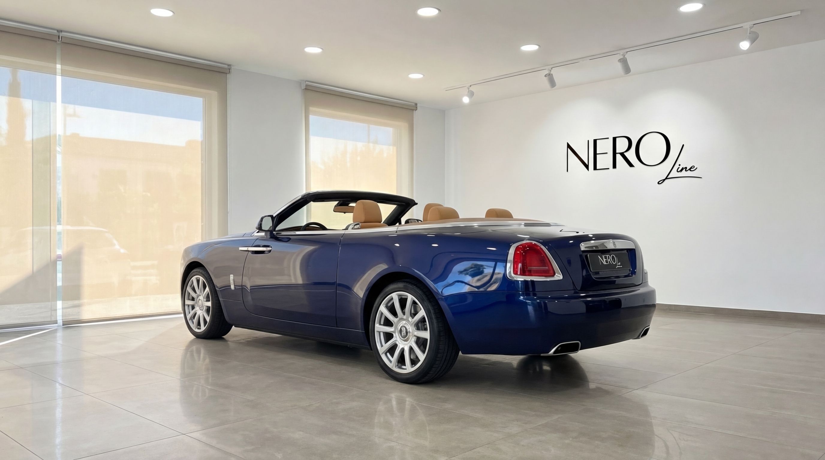 The midnight blue 2024 Rolls-Royce Dawn convertible is parked in a showroom, showing its rear three-quarter view with the top down in Barcelona.