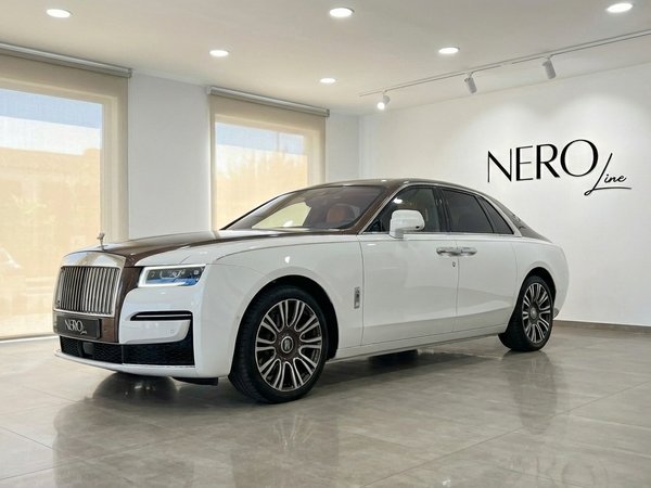 Rolls-Royce Ghost Amber Roads — Sedán de Lujo Madrid El sedán de lujo Rolls-Royce Ghost Amber Roads blanco y marrón 2024 está aparcado en el interior en Madrid, visto desde un ángulo frontal de tres cuartos.