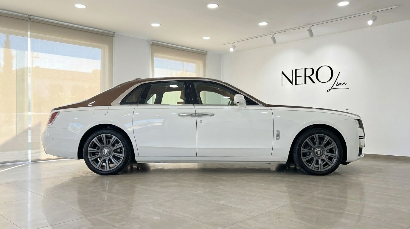 El sedán de lujo Rolls-Royce Ghost Amber Roads 2024 blanco y marrón está estacionado en una sala de exposición en Madrid.