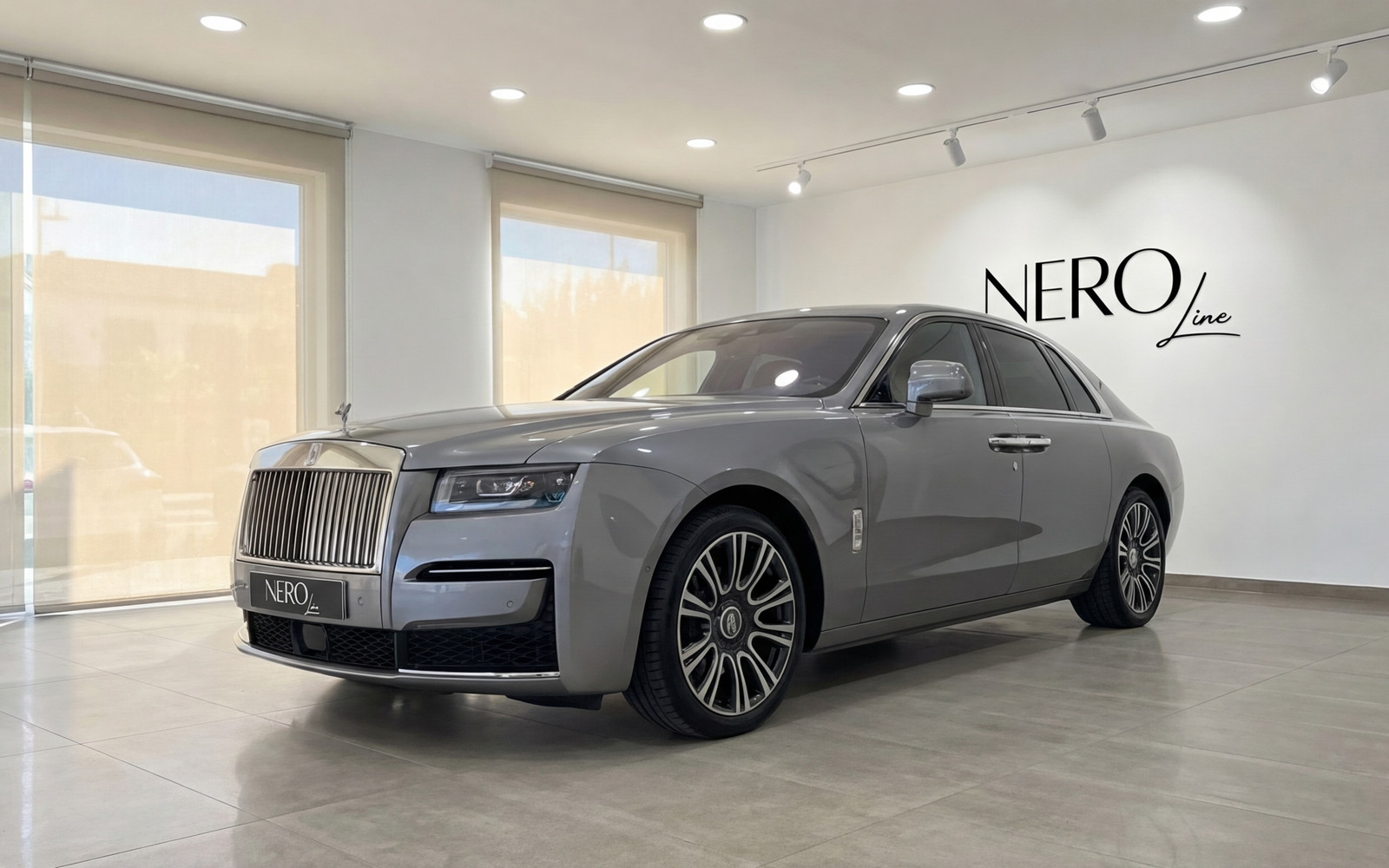 Rolls-Royce Ghost — Luxury sedan in Valencia The metallic gray Rolls-Royce Ghost is elegantly parked in a showroom, showcasing its luxurious front three-quarter view in Valencia.