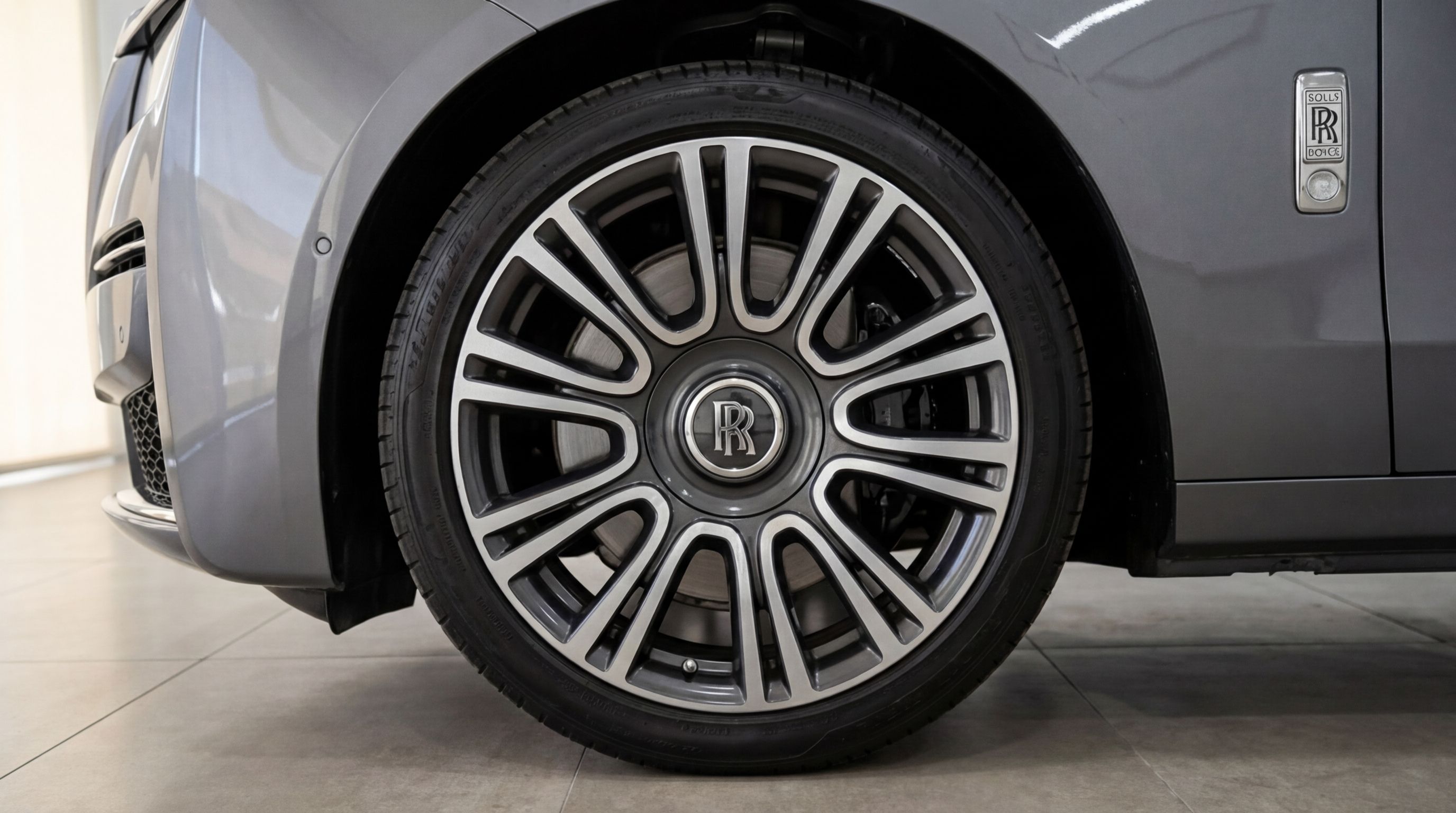 The metallic gray Rolls-Royce Ghost features a detailed view of its front wheel, tire, and iconic 'RR' badge in Valencia.