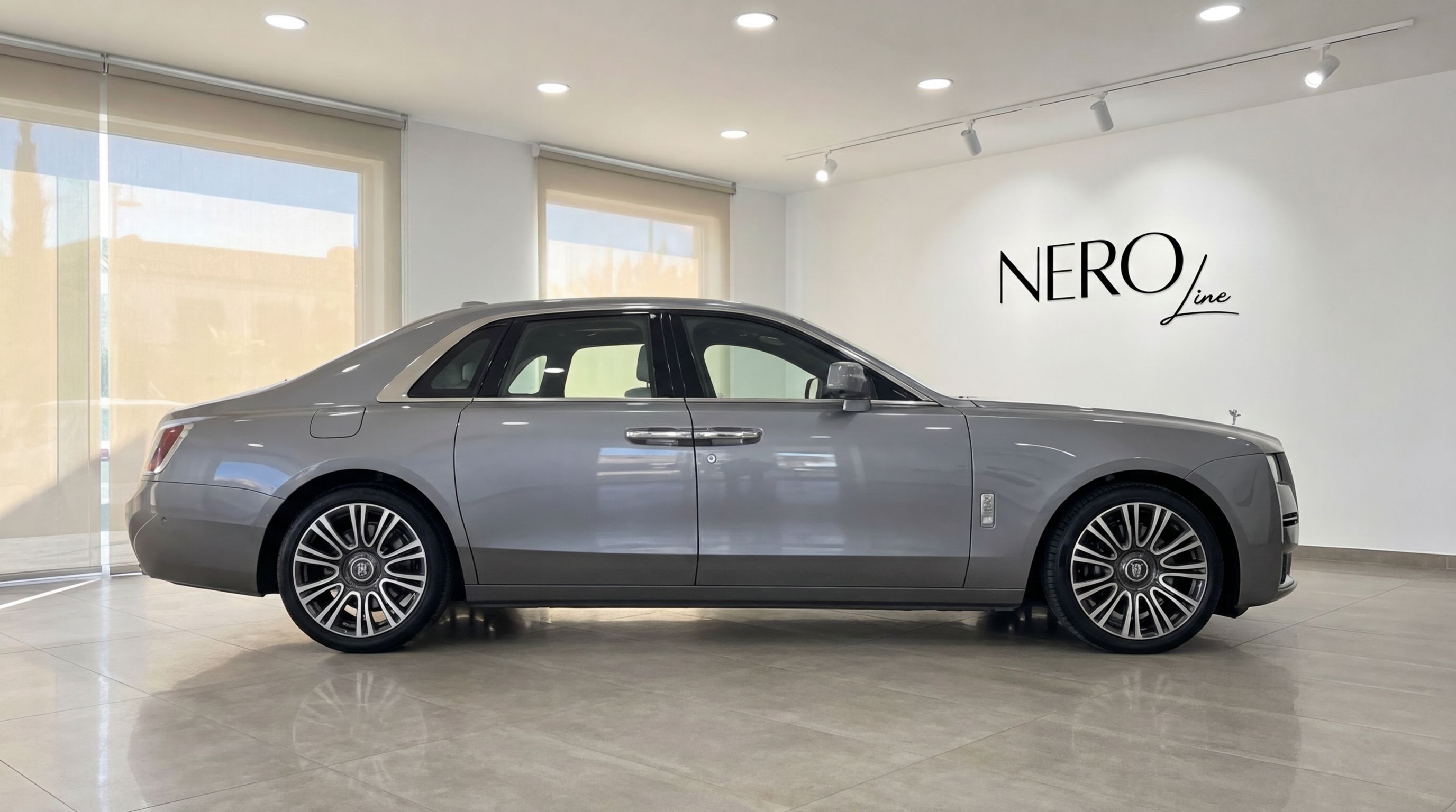 La berline de luxe Rolls-Royce Ghost 2024 gris métallisé est exposée dans un showroom, vue de son élégant profil à Madrid.