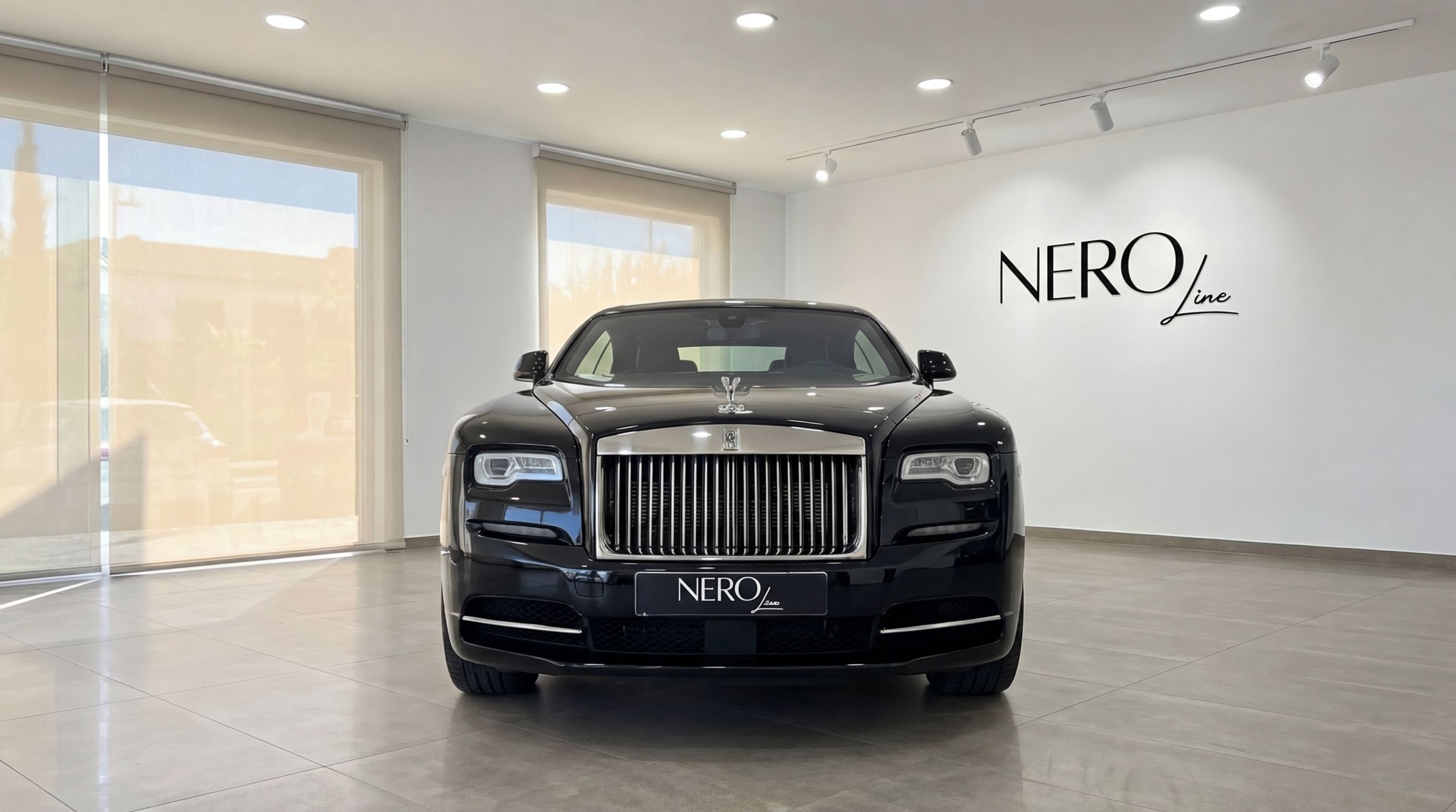 The jet black Rolls-Royce Wraith is prominently displayed from a front view in a modern showroom in Malaga.