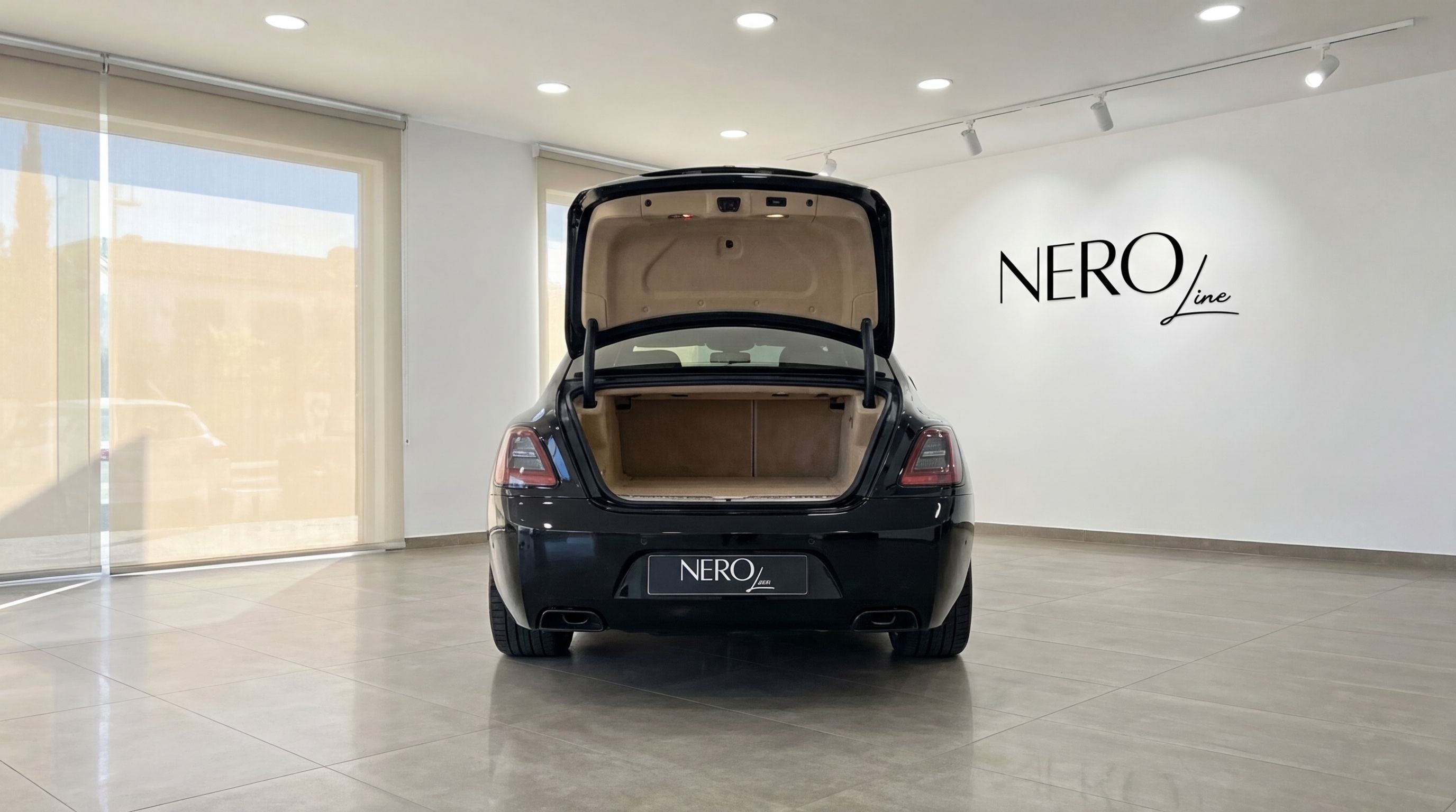 Rear view of the jet black Rolls-Royce Wraith with its trunk open, showcasing the spacious interior in a Malaga showroom.