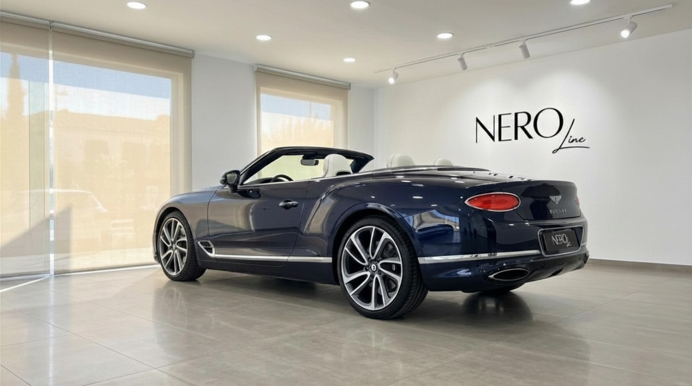 Bentley Continental GTC convertible in Gloss Dark Sapphire Blue, shown from the rear three-quarter angle with the top down, displayed in a showroom in Barcelona.