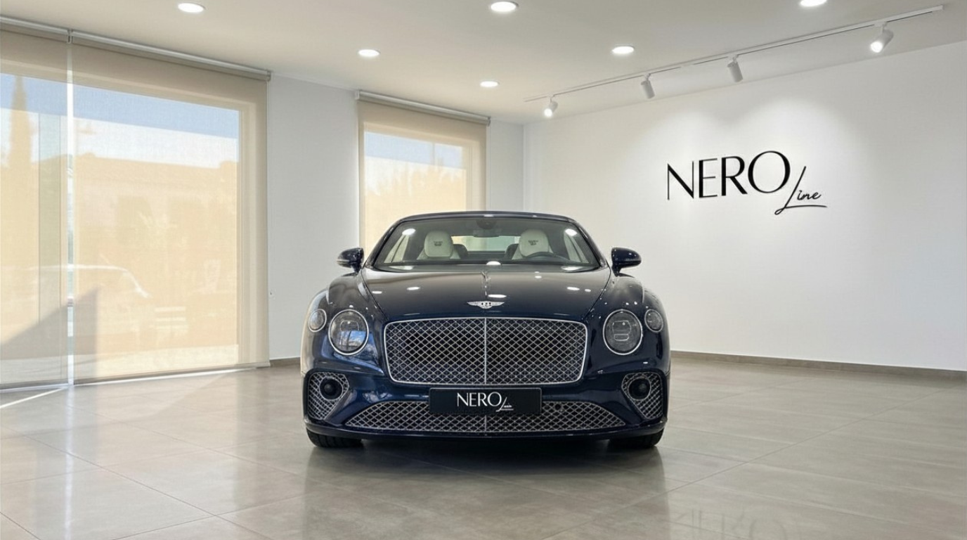 The Gloss Dark Sapphire Blue Bentley Continental GTC Speed W12 is showcased from the front in a bright Barcelona showroom.